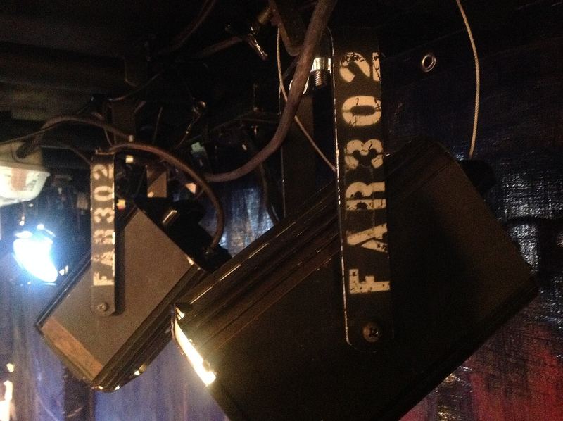Twee zwarte theaterspots aan een buis boven een podium, met de naam van het theater op de beugels.